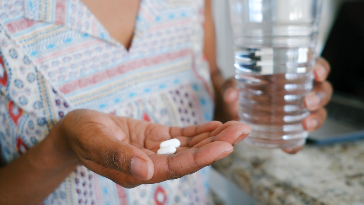 Close-up of a woman&#039;s hands, one holding two oblong white tablets, resembling tylenol, and the other holding a glass of water