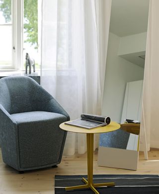 Full-length mirror beside a blue chair with an open magazine on the table