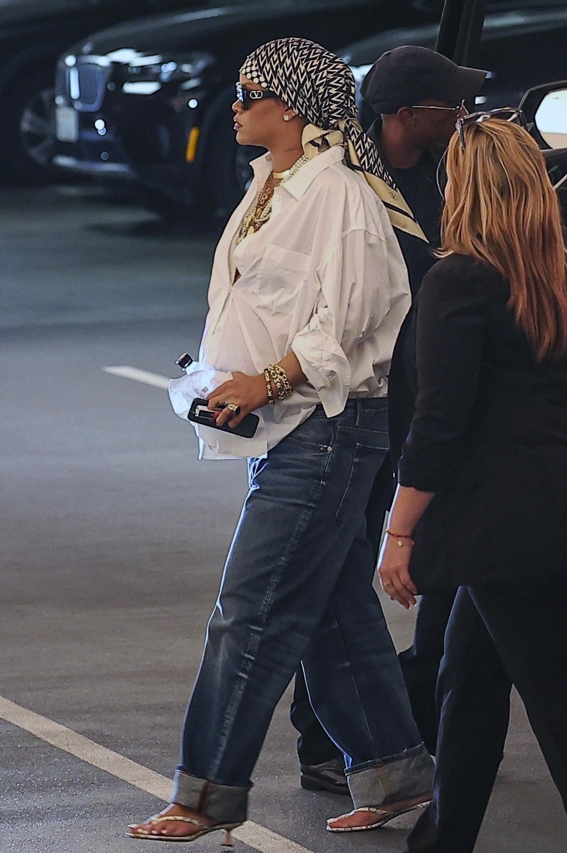 Rihanna walks into a Los Angeles office building wearing an oversize button down with jeans and a scarf over her hair