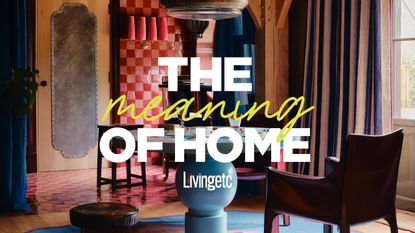 A colorful living room with a lacquered pale blue round table, mismatched leather chairs, a checkerboard wall in tones of pink, and pale blue-washed wooden beams, overlaid with "meaning of home" logo