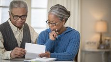 An older couple looks at paperwork while sitting at their dining room table.