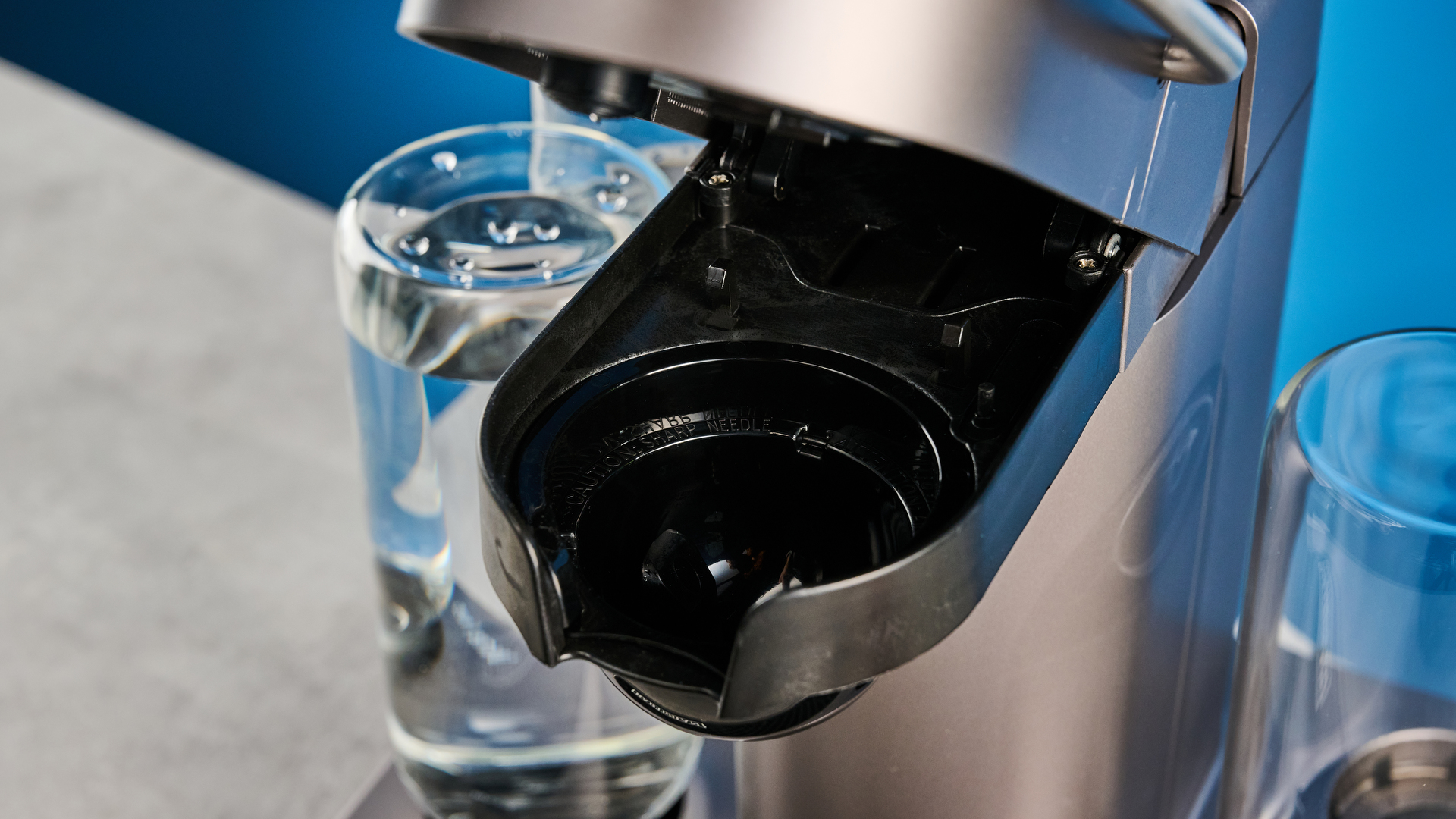the bartesian premium cocktail machine photographed against a blue background showing its drink-making abilities and accessories and functionality with cocktail pods