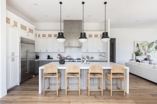 A white kitchen with a large island, rattan bar stools, and three black pendant lights hanging overhead