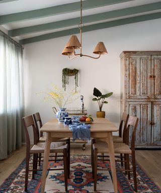 sage green painted ceiling beams over a kitchen diner with a blue and red colorful rug