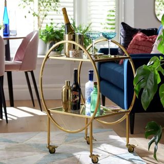 gold drinks trolley with bottles of alcohol in front of a navy blue sofa
