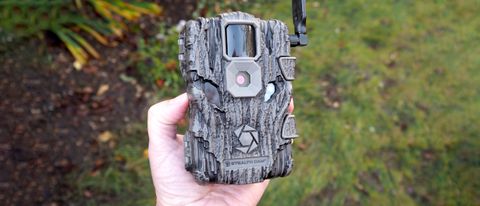 Stealth Cam Fusion Global Trail Camera held in a hand over grass