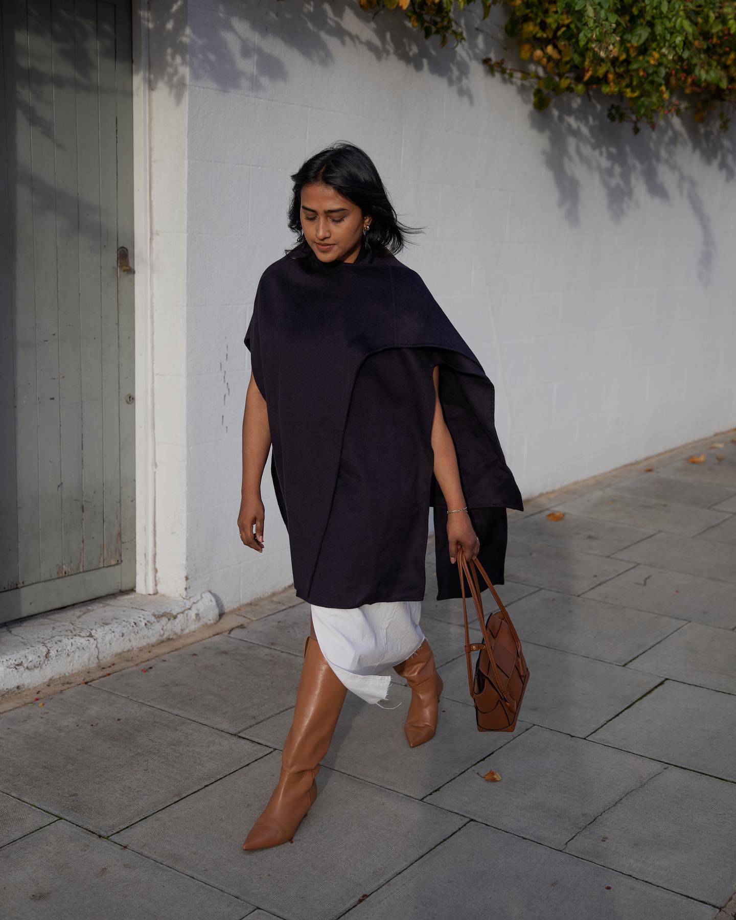 An image of @chiarasatelier wearing cowboy boots with a white skirt and black cape top.