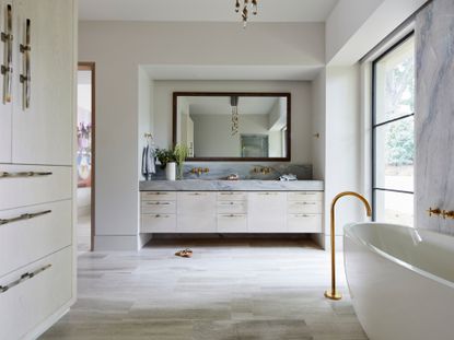 neutral bathroom with freestanding tub, stone splashbacks, vanity unit and pale wood flooring 