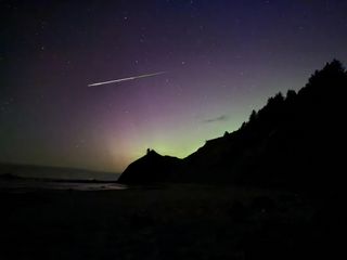 a long colorful meteor streak through the sky with a distinct green glow toward the end of the tail meanwhile the sky glows green and purple during the aurora display.