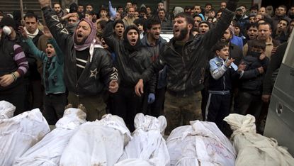 Syrians shout slogans as they gather around the shrouded bodies of civilians, who were executed and dumped in the Quweiq river, during their funeral outside the Yarmuk school in the Bustan al