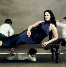 Ashley Graham wears a blue satin gown lying on a couch as her three sons run around her 