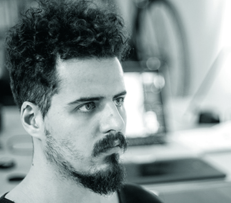 Artist headshot; a young bearded man with curly hair