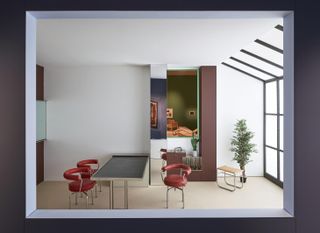 A studio apartment. Large, black framed windows to the right cover the entire wall and a part of the ceiling. A silver metal table with a black top stands between three red leather chairs.