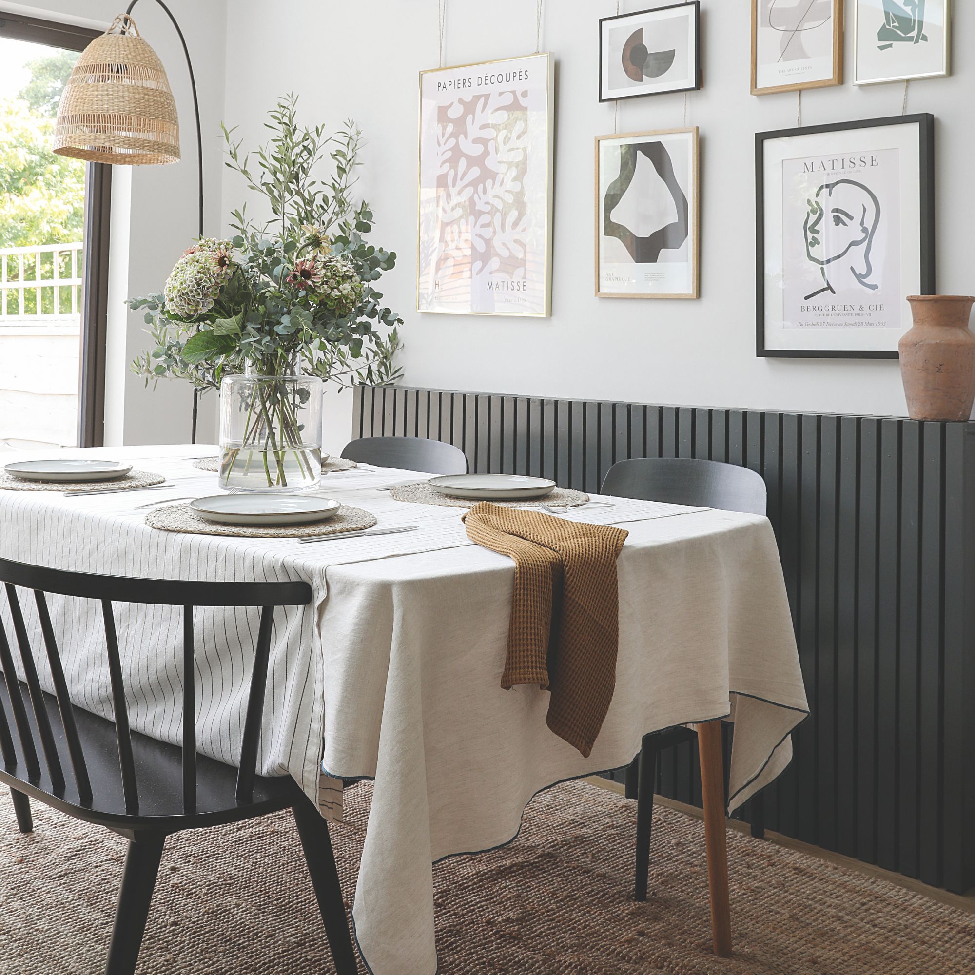A dining room with a rectangular table covered with a white tablecloth, a gallery wall behind it and a rug on the floor