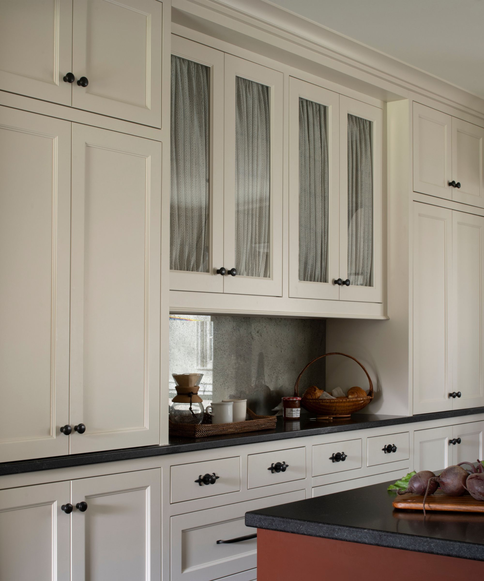 A white kitchen with a rust-red island and glazed cabinets with fabric lining