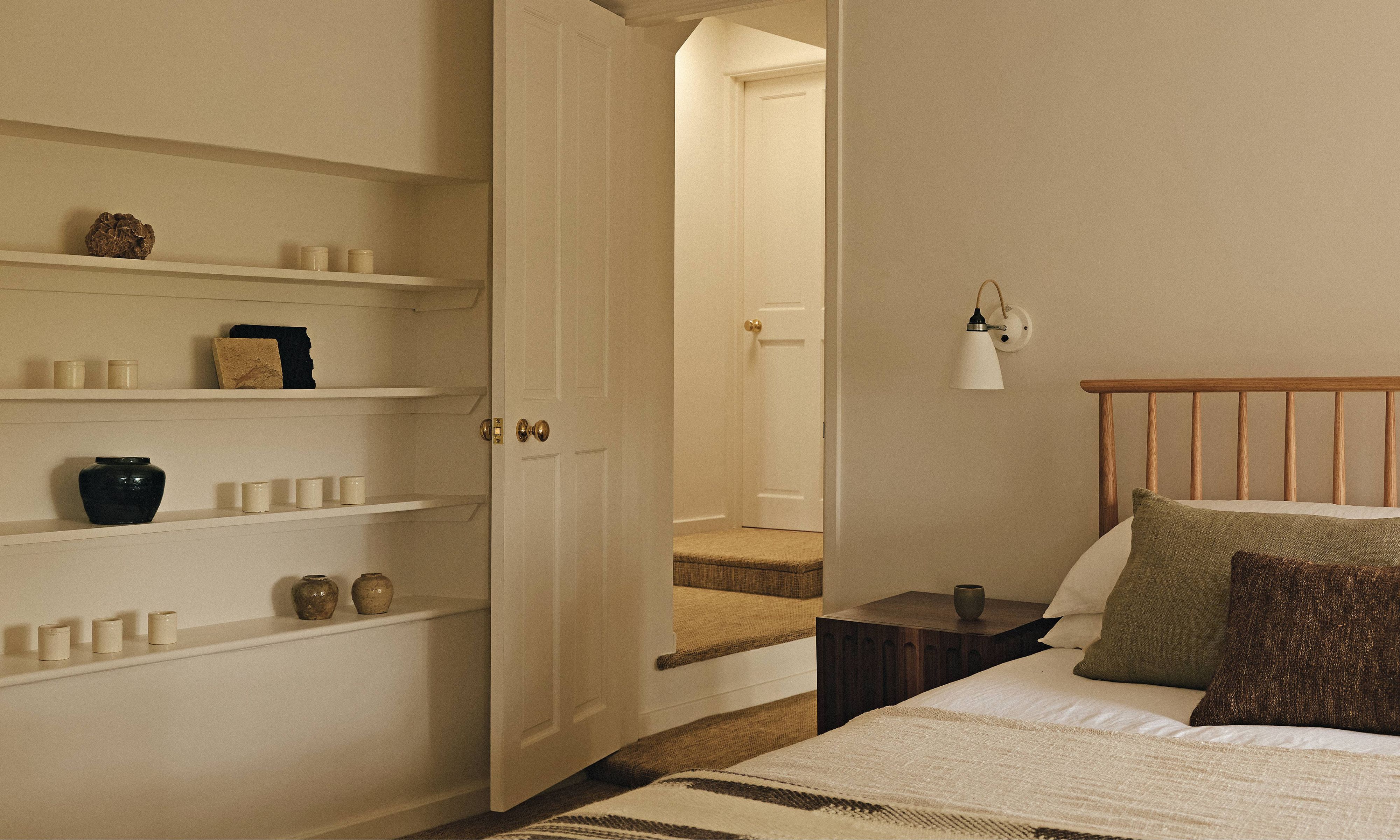 a neutral large bedroom with built in shelving filled with vintage pottery with a danish wooden bed and earthy linens