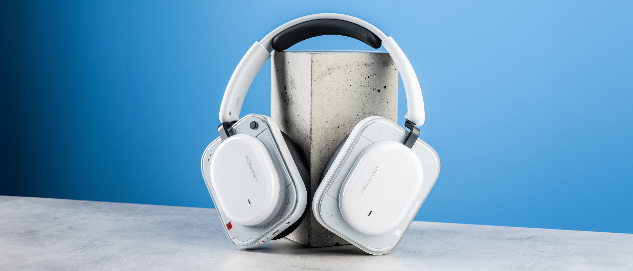the nothing headphone (a) photographed against the blue tom's guide background, showing the transparent and white ear cups with red accents, the padded headband, and the accessories including 3.5mm jack