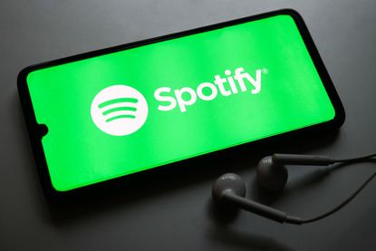 Green Spotify logo on smartphone with airpods next to it
