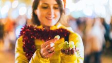 A woman in a yellow coat with red tinsel around her neck eats grapes outside during New Year's Eve festivities in Spain