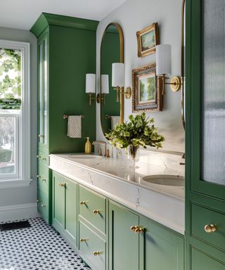 traditional bathroom with mid green cabinets, wall sconces and gold mirror and photo frames on the wall