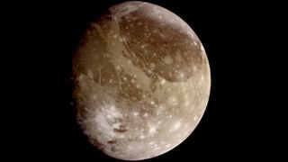 Ganymede imaged by NASA's Galileo spacecraft appearing as a sandy brown colored cratered moon. with the left portion partly in shadow.