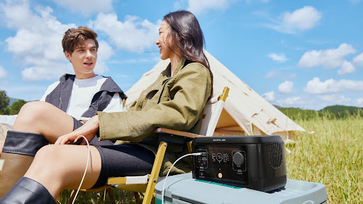 A young man and woman sitting on a blanket outside, with a tablet computer and an EcoFlow RIVER mini Portable Power Station in front of them.
