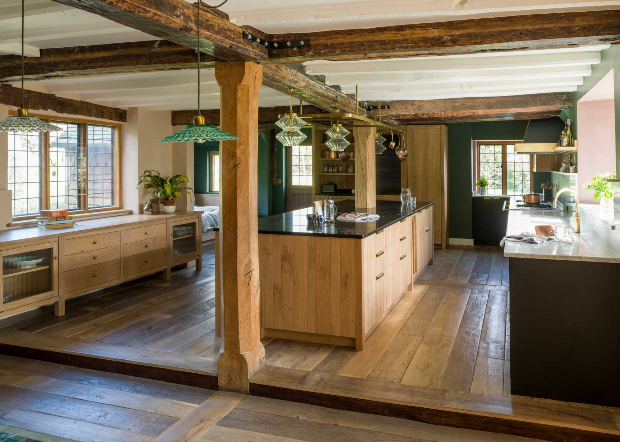 rustic kitchen with wooden beams, wooden cabinetry, and wooden flooring. Glass pendant lights hang above he central kitchen island