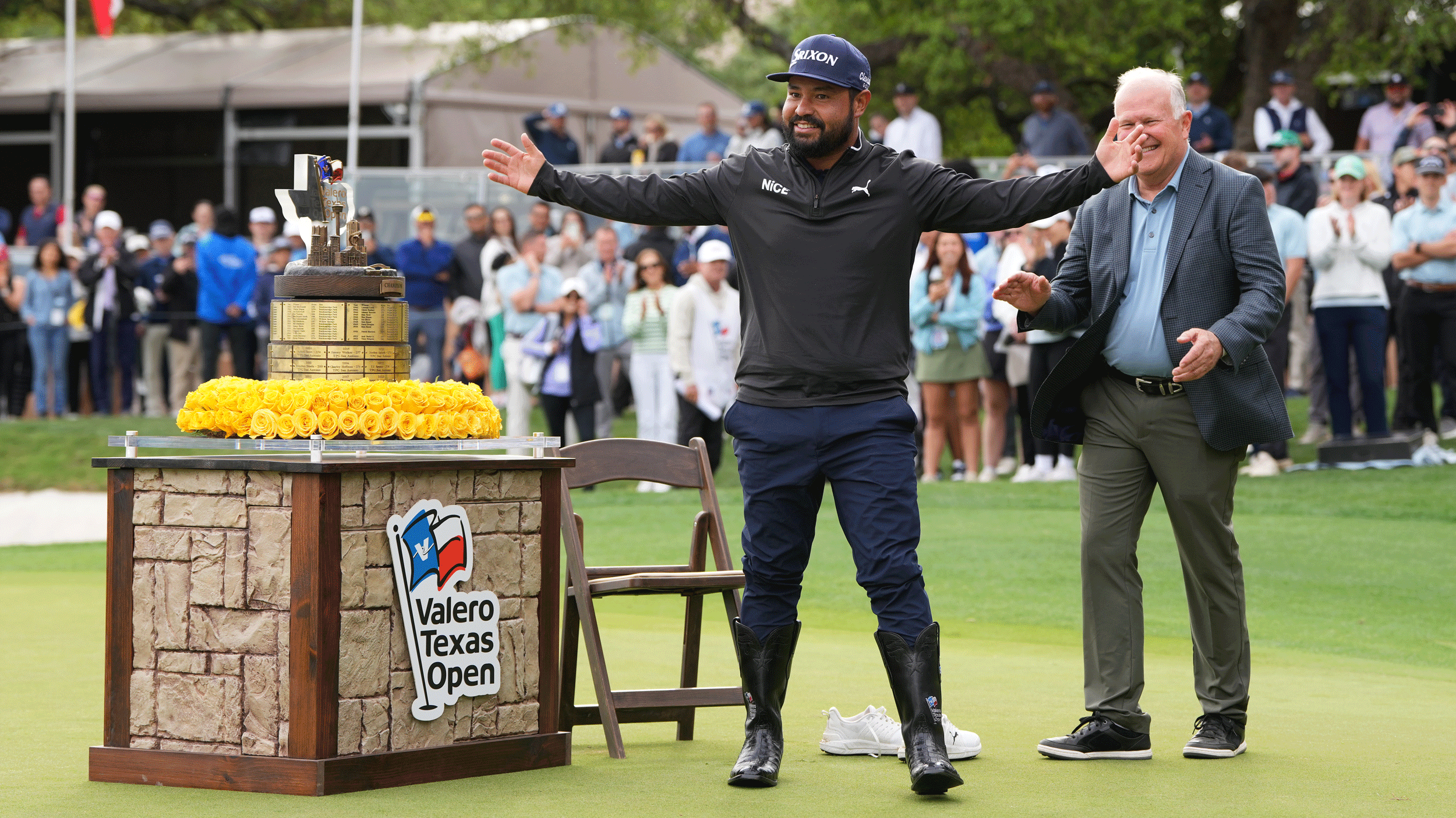JJ Spaun spreads his arms out wide in front of the trophy after putting on cowboy boots, a prize he earned after winning the 2026 Valero Texas Open