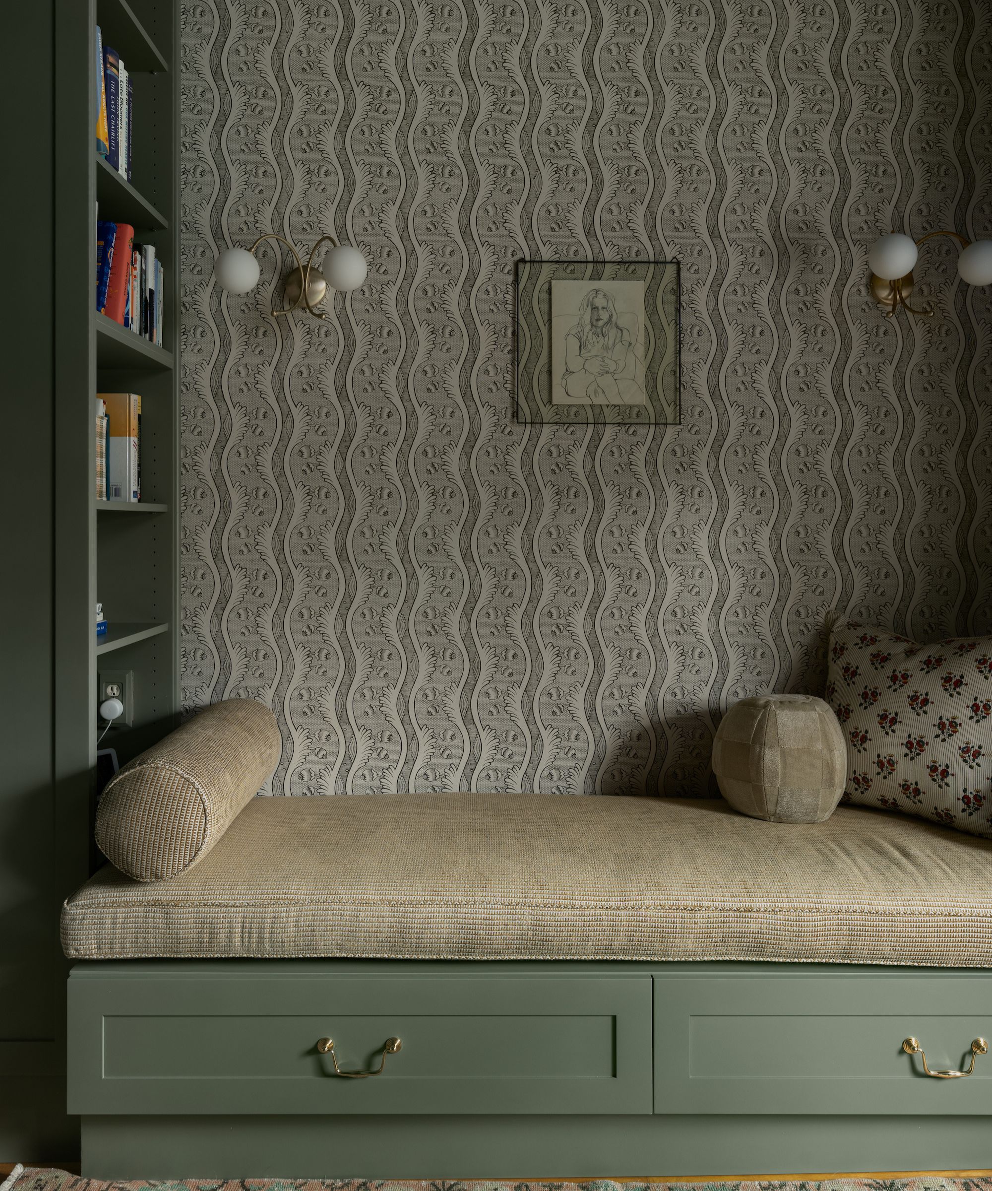 Reading corner with built-in bookcase and built-in daybed with storage drawers underneath, green topper and bolster cushion and floral striped wallpaper with sconces and vintage print