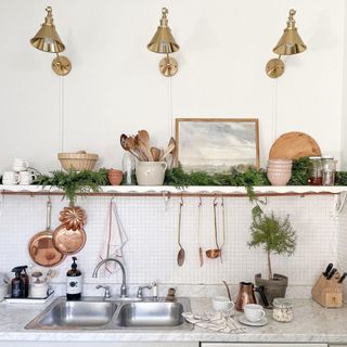 Metallic accents with brass wall lights and hanging copper pans and utensils in white kitchen scheme.