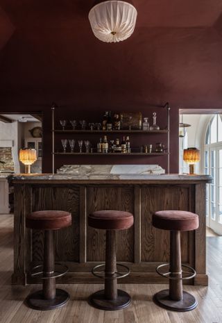 Red walls, and velvet barstool covers, marble counter top, metal shelves