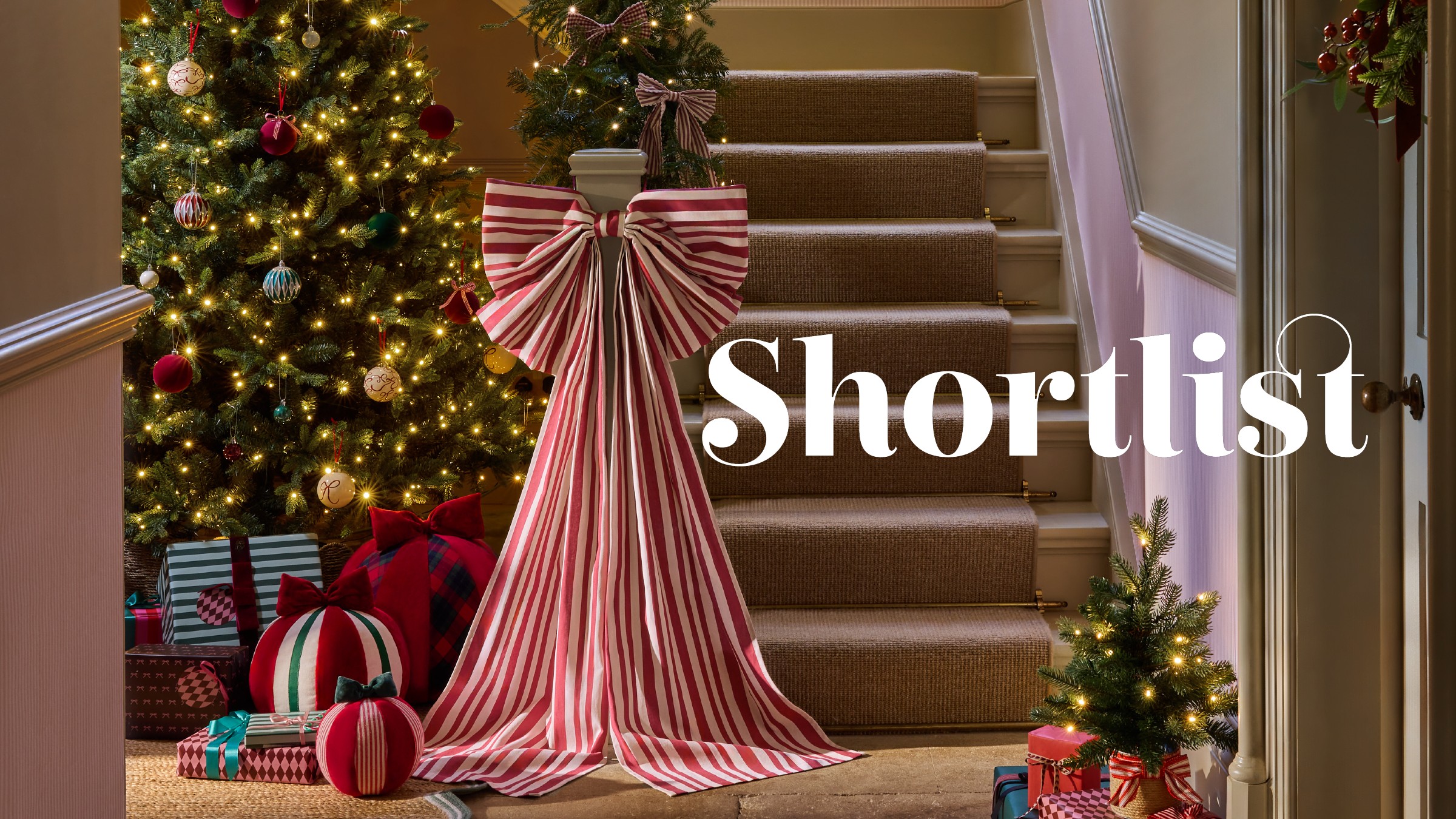 A hallway with a staircase decorated for Christmas with a big red striped bow from Next and a lit-up Christmas tree