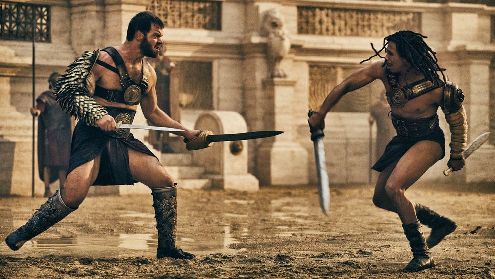 Viggo (Jóhannes Haukur Jóhannesson) and Kwame (Moe Hashim) decked out in gladiator gear as they face off in the arena in &quot;Those About to Die&quot;