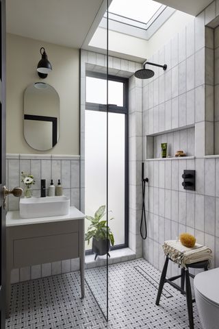 small bathroom with shower, glass door, marble floor and walls, small vanity, black fixtures and fittings