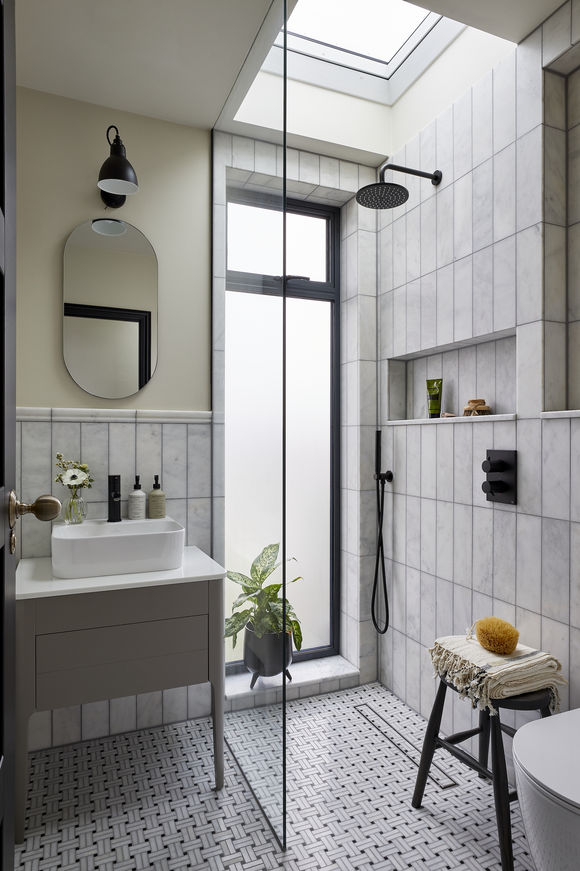 petite salle de bain avec douche, porte vitrée, sol et murs en marbre, petite vasque, luminaires et accessoires noirs