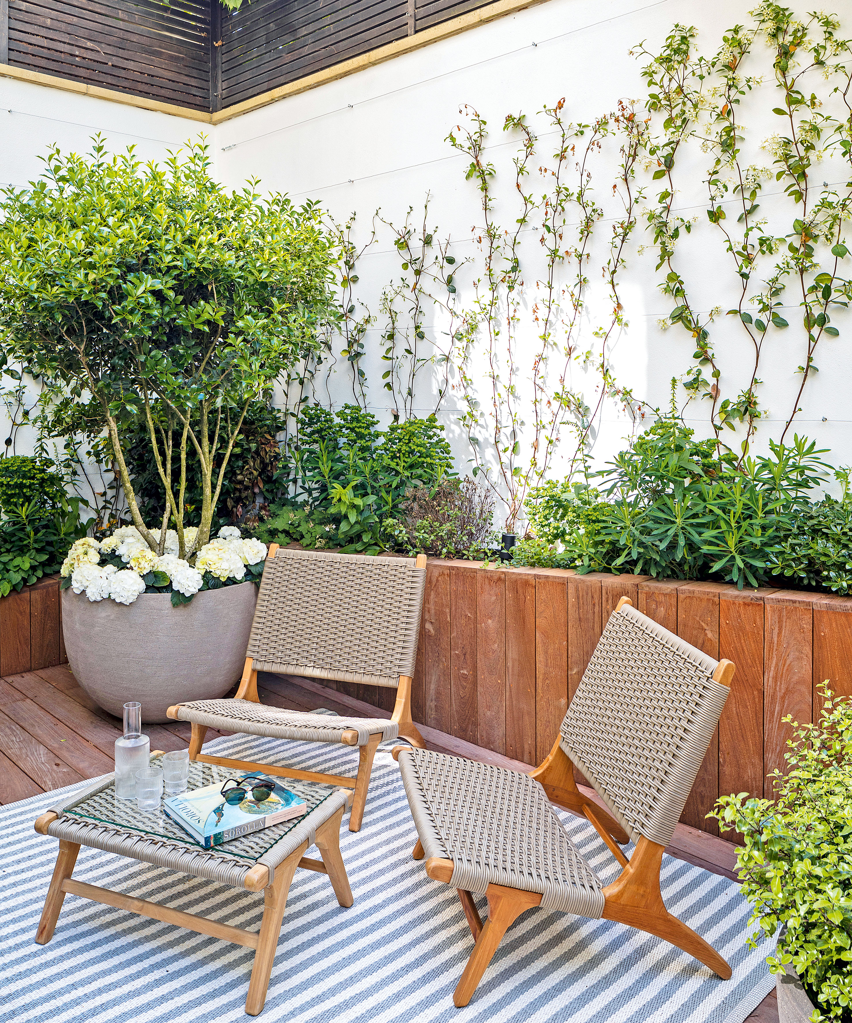 small walled courtyard with wooden planters, seating and rug