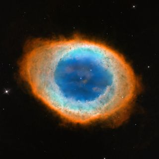 This close-up, visible-light view by NASA's Hubble Space Telescope reveals new details of the Ring Nebula. The object is tilted toward Earth so that astronomers see the ring face-on. The Hubble observations reveal that the nebula's shape is more complicated than astronomers thought. The blue gas in the nebula's center is actually a football-shaped structure that pierces the red doughnut-shaped material. Image released May 23, 2013.