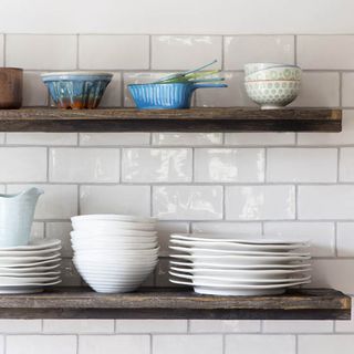 kitchen area with white wall tiles and wooden shelf on wall with white dish and bowls.