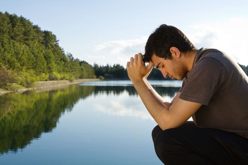 Man prays by a lake.