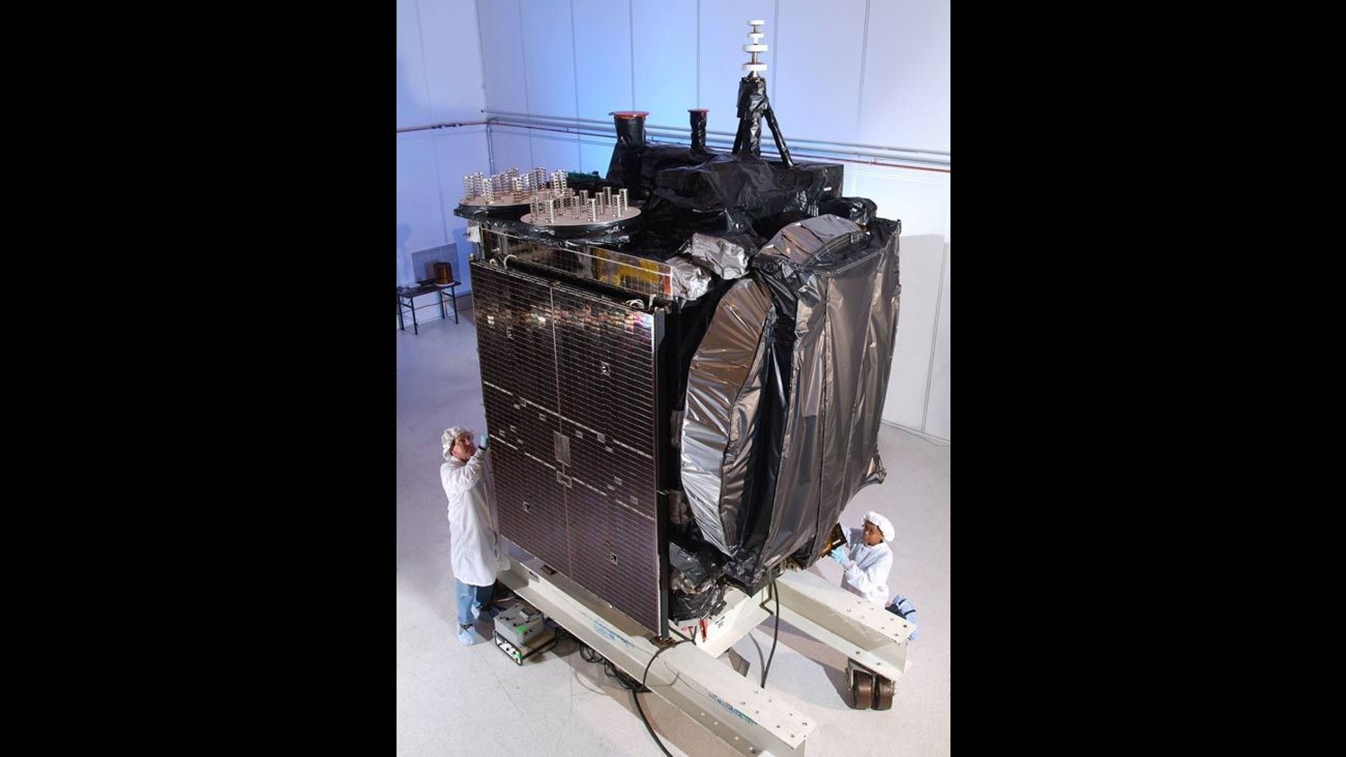 satellite sitting on cart with two technicians alongside in white suits
