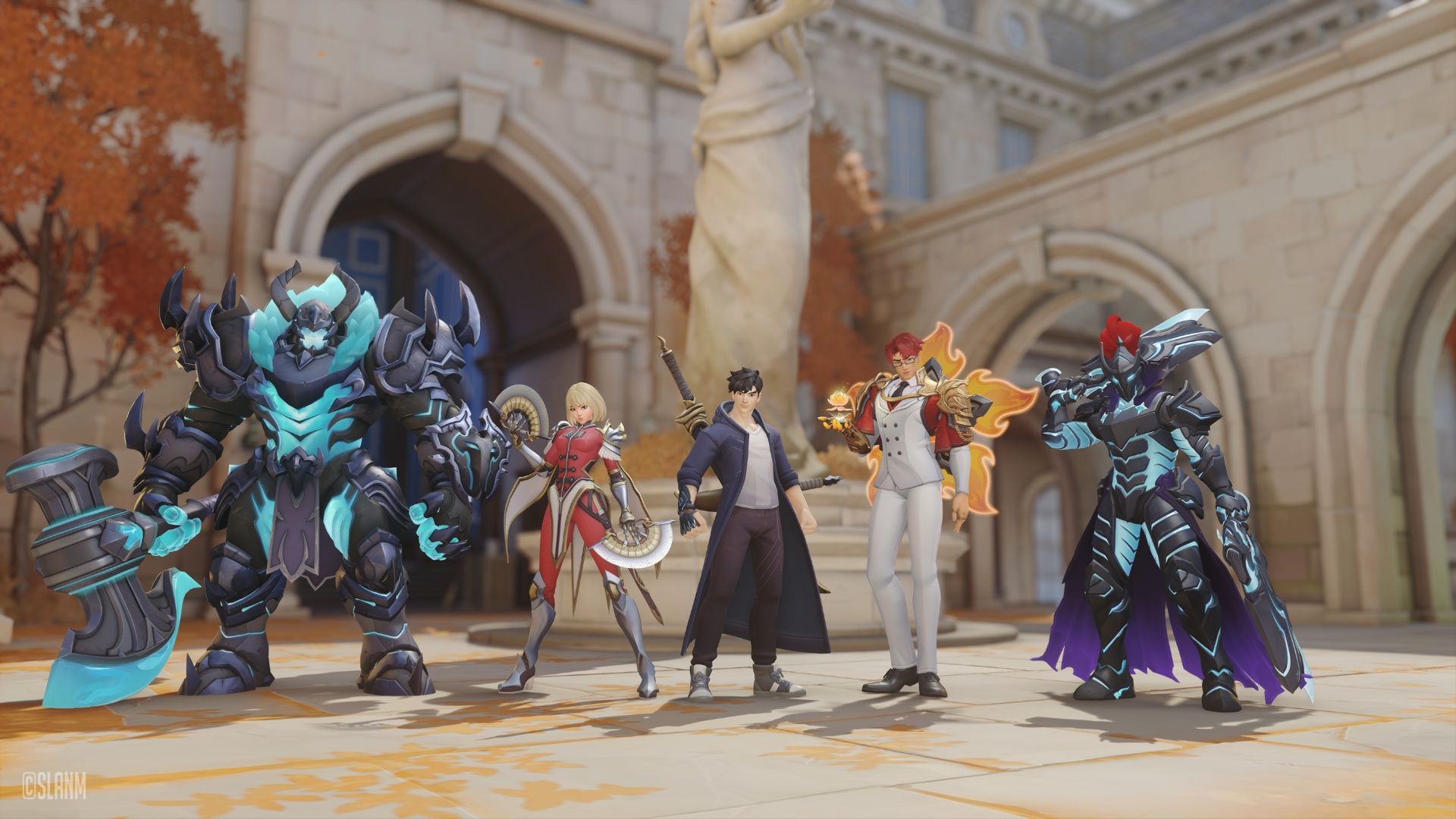 A video game team poses in a stone courtyard beneath a statue, flanked by towering armored warriors; autumn leaves add a dramatic fantasy tone.