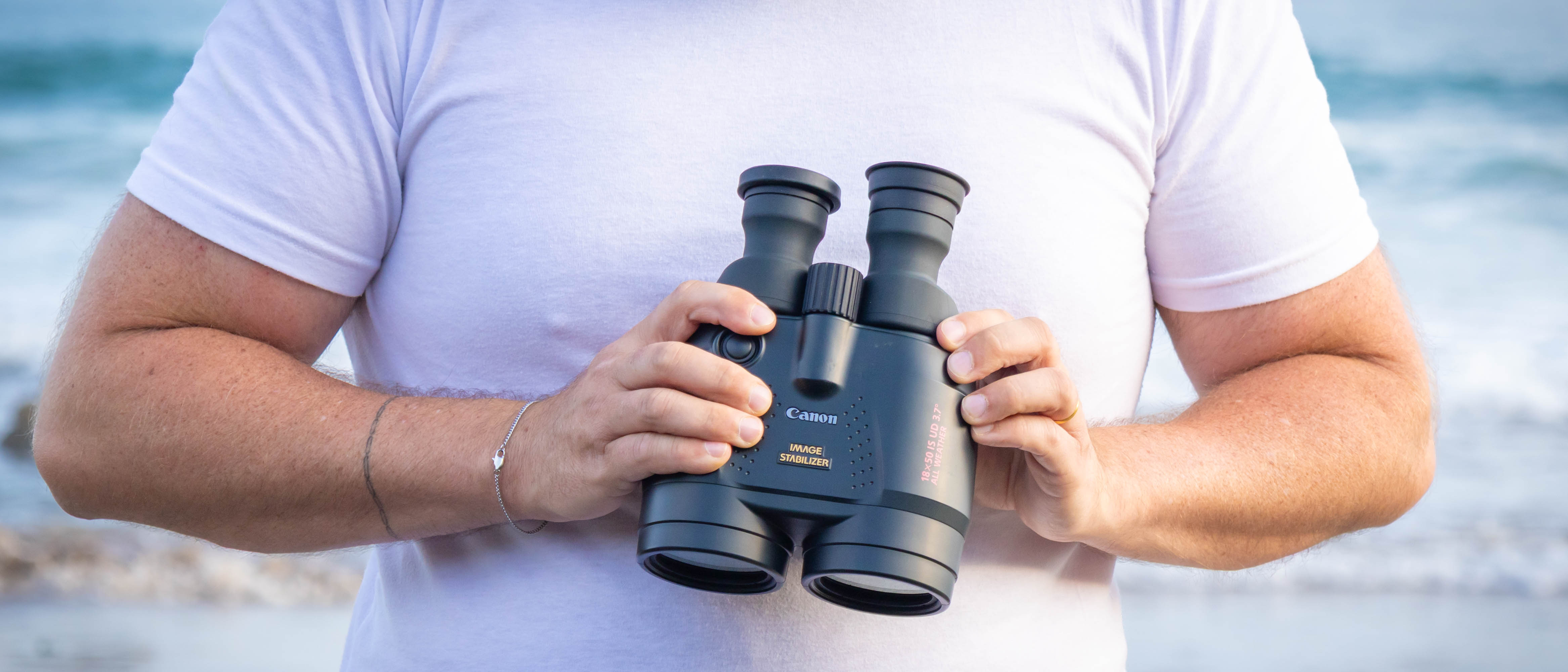A person holding the Canon 18x50 IS binoculars at their chest level, showing the top of the binoculars.