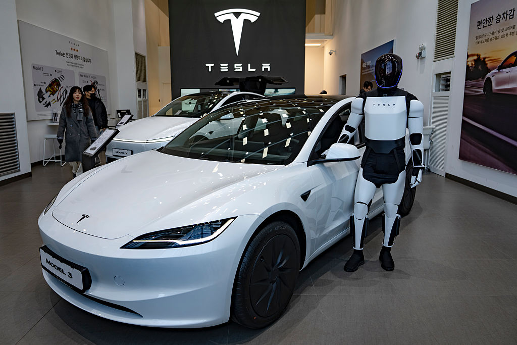 A person dressed in a Tesla Optimus humanoid robot costume poses next to the newly released Tesla Model 3 at the Tesla showroom in Yeouido, Seoul, on January 31, 2026