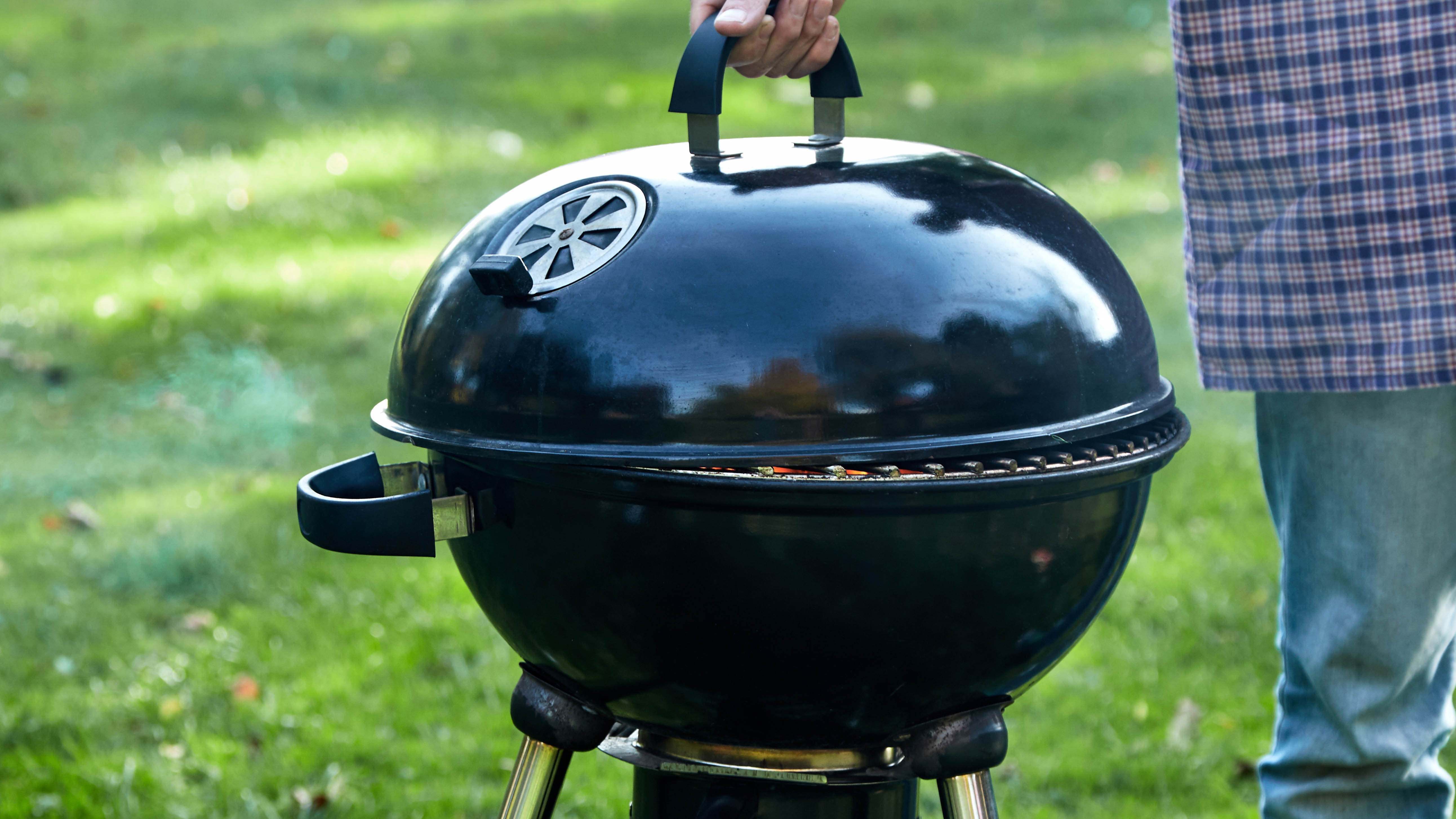 A man putting a lid on top of the barbecue