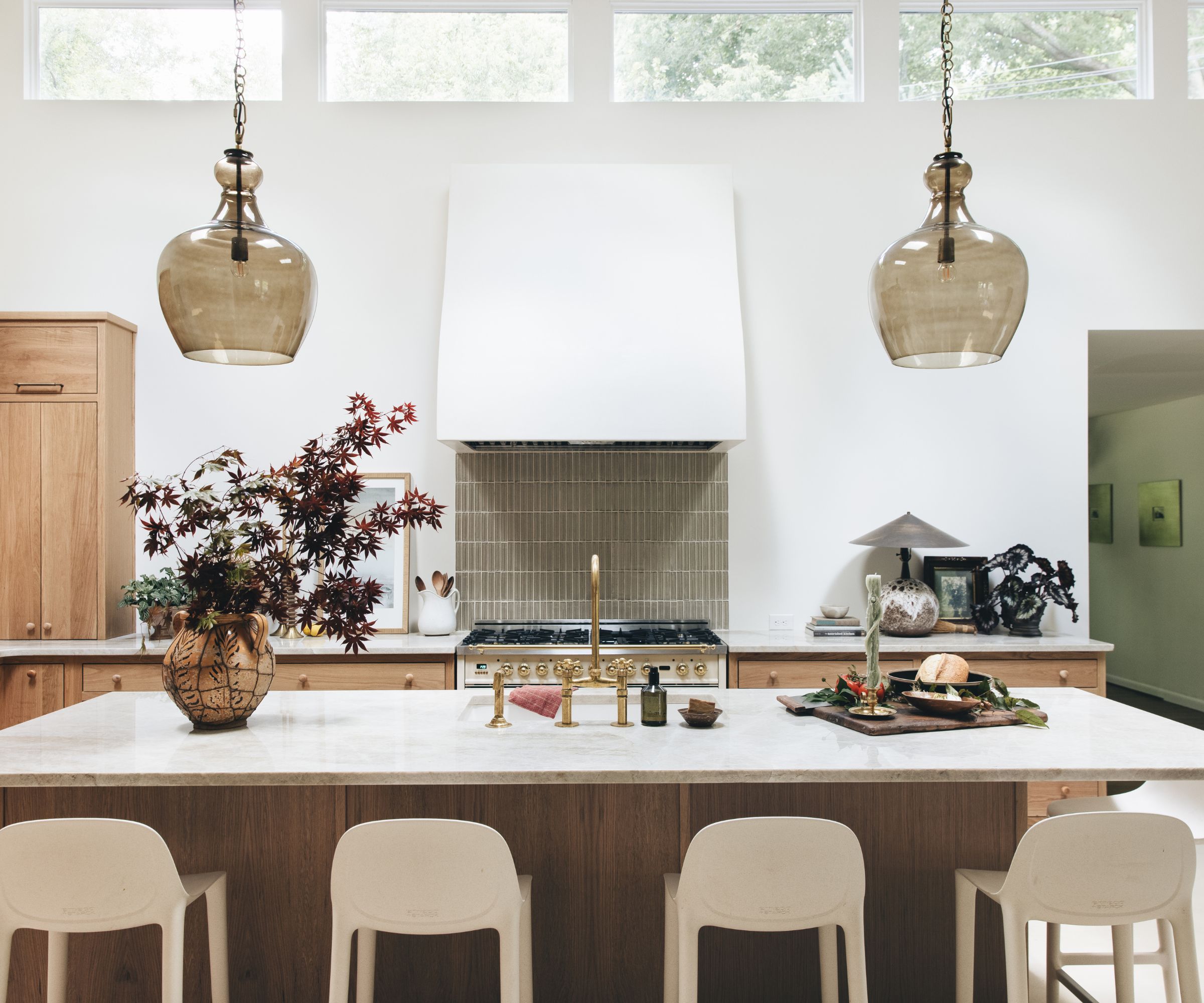 A kitchen with a large island, wooden cabinets, marble countertops, and a tiled backsplash