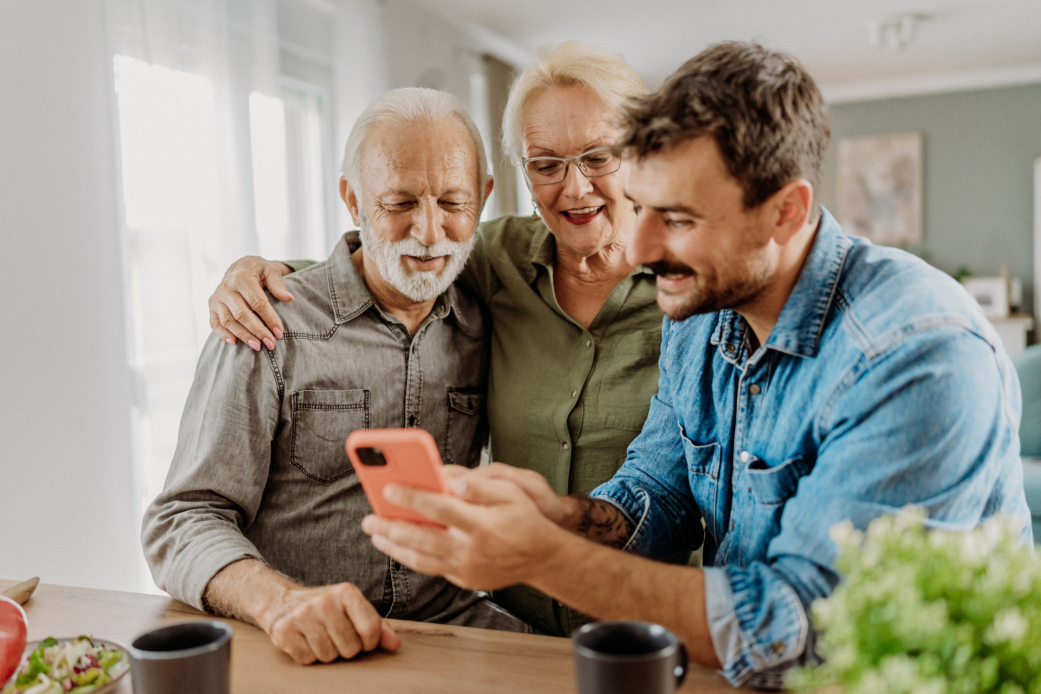 Son visiting his parents, showing them photos on his smartphone.