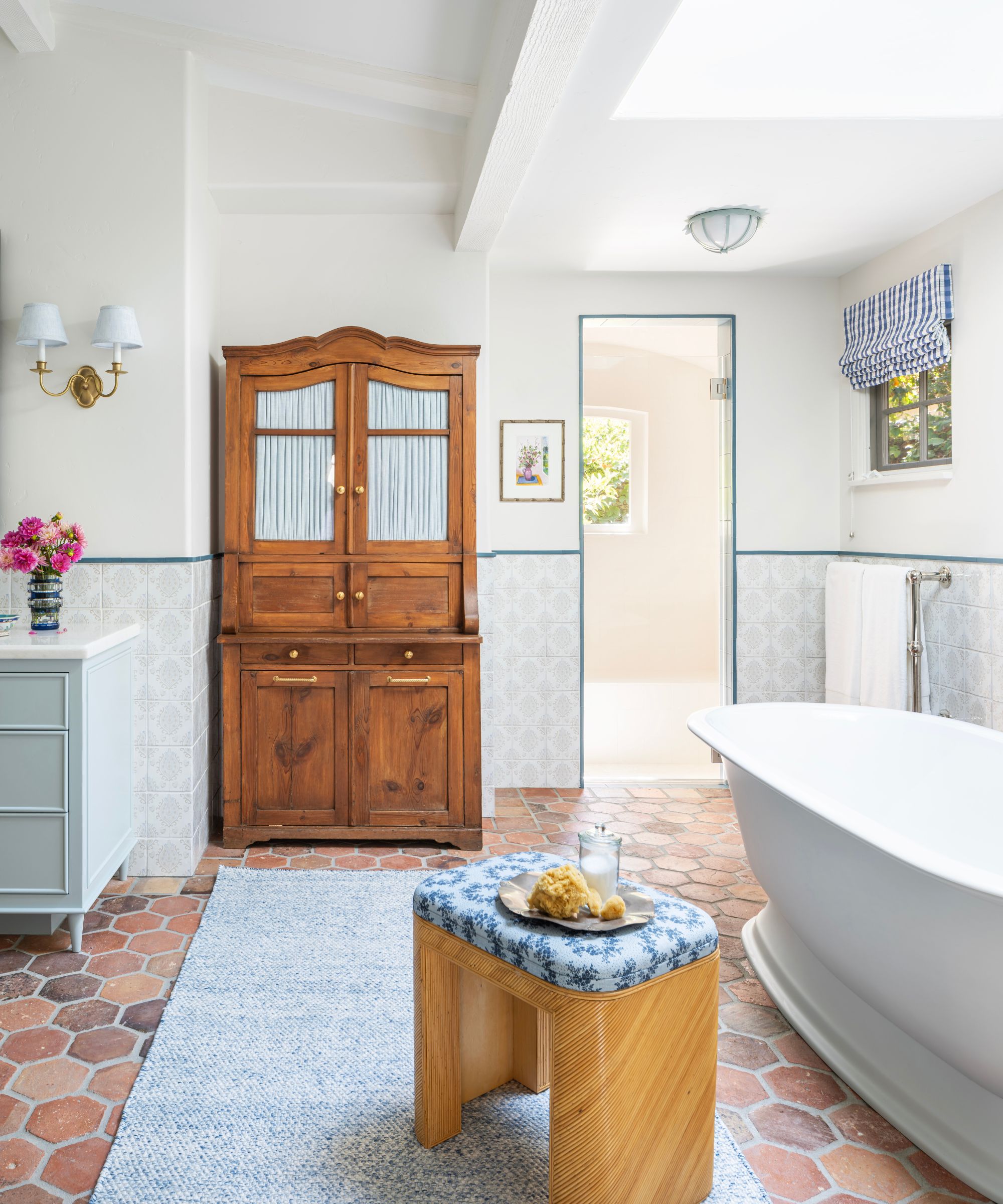 A large bathroom with white walls, a blue vanity, a wooden cabinet, terracotta floor tiles, and vintage-inspired patterned wall tiles