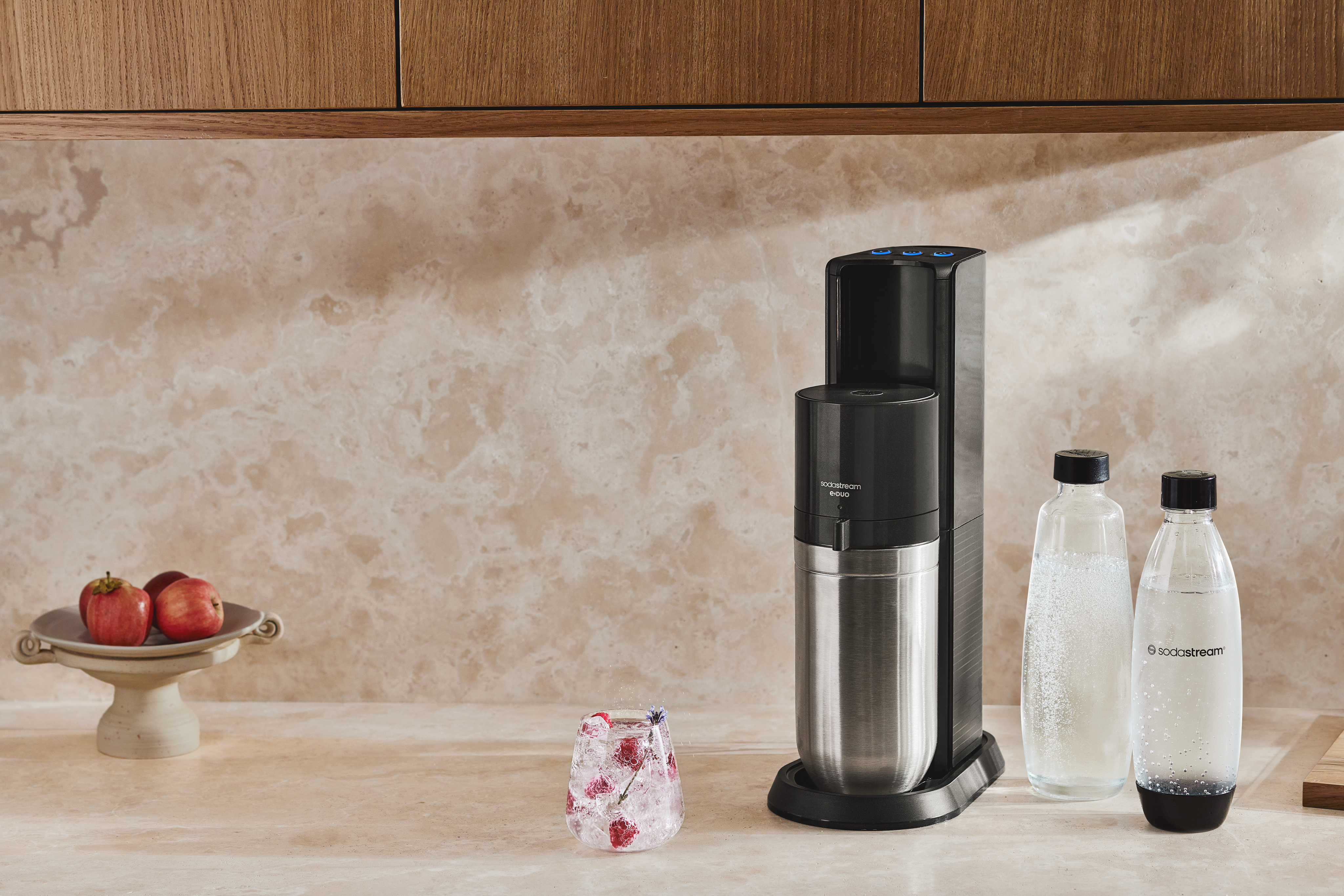 SodaStream E-Duo på en køkkenbordplade af sten ved siden af en glas- og plastflaske