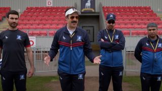 From left to right: Roy standing still, Ted talking to the team, Beard standing with his arms crossed and Nate standing with his arms behind his back.