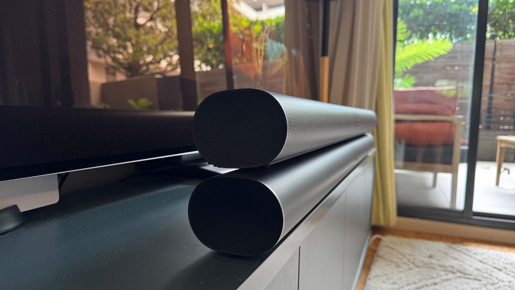 Angled Side view of Sonos Arc on top of Sonos Arc Ultra on a blue TV bench